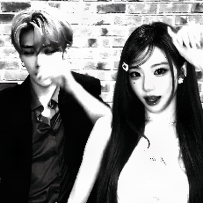 A Man And A Woman Are Standing Next To Each Other In Front Of A Brick Wall In A Black And White Photo . GIF