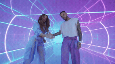 A Man And A Woman Are Standing Next To Each Other In Front Of A Neon Tunnel GIF