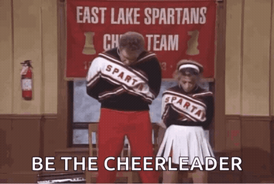 A Man And A Woman Are Standing Next To Each Other In Front Of A Sign That Says East Lake Spartans Cheerleading Team . GIF