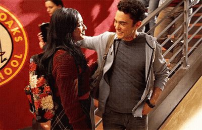 A Man And A Woman Are Standing Next To Each Other In Front Of A Sign That Says Oak 'S School GIF