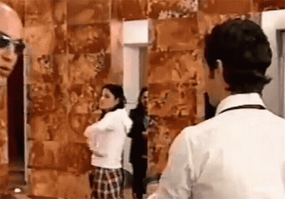 A Man And A Woman Are Standing Next To Each Other In Front Of A Wall Covered In Pictures . GIF