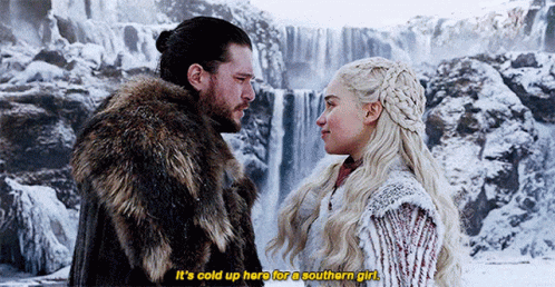 A Man And A Woman Are Standing Next To Each Other In Front Of A Waterfall In The Snow . GIF