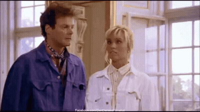 A Man And A Woman Are Standing Next To Each Other In Front Of A Window GIF