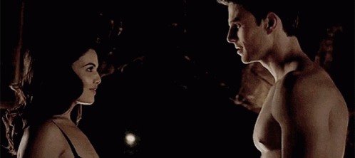 A Man And A Woman Are Standing Next To Each Other In The Dark Looking At Each Other . GIF