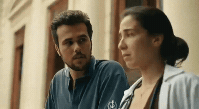 A Man And A Woman Are Standing Next To Each Other Looking At Each Other . GIF