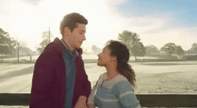 A Man And A Woman Are Standing Next To Each Other On A Balcony And Kissing . GIF