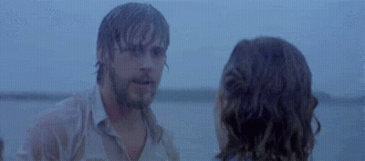 A Man And A Woman Are Standing Next To Each Other On A Beach Looking At Each Other . GIF