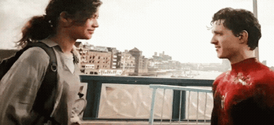 A Man And A Woman Are Standing Next To Each Other On A Bridge Looking At Each Other . GIF