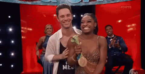 A Man And A Woman Are Standing Next To Each Other On A Stage Holding A Gold Medal . GIF