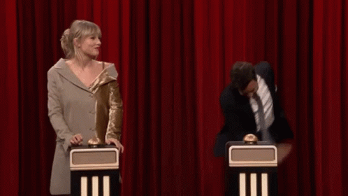 A Man And A Woman Are Standing Next To Each Other On A Stage With A Red Curtain Behind Them . GIF