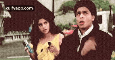 A Man And A Woman Are Standing Next To Each Other On A Street . The Man Is Pointing At The Woman . GIF