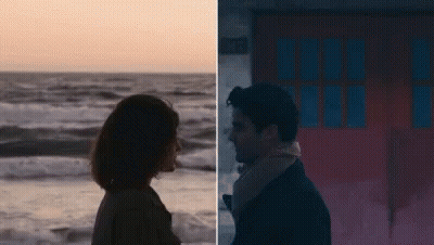 A Man And A Woman Are Standing Next To Each Other On The Beach And Looking At Each Other . GIF