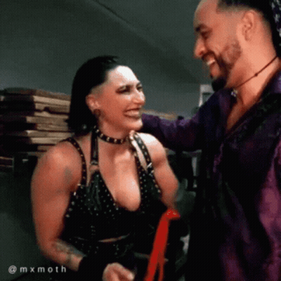 A Man And A Woman Are Standing Next To Each Other Smiling And Laughing . GIF