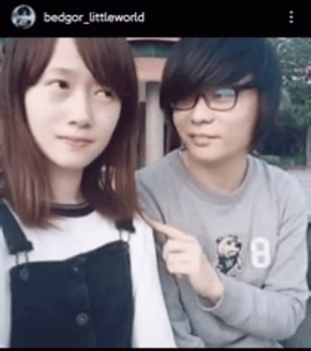A Man And A Woman Are Standing Next To Each Other . The Woman Is Pointing At The Man 'S Arm . GIF