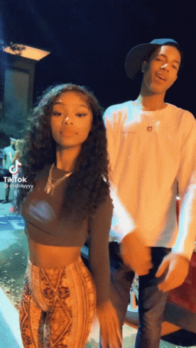 A Man And A Woman Are Standing Next To Each Other . The Woman Is Wearing A Crop Top And Pants . GIF