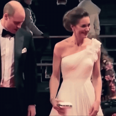 A Man And A Woman Are Standing Next To Each Other . The Woman Is Wearing A White One Shoulder Dress . GIF