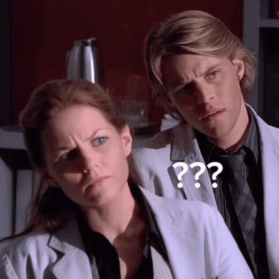 A Man And A Woman Are Standing Next To Each Other With A Question Mark On The Man 'S Jacket GIF
