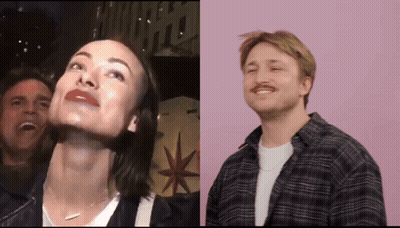 A Man And A Woman Are Standing Next To Each Other With A Sign That Says Hollywood In The Background GIF