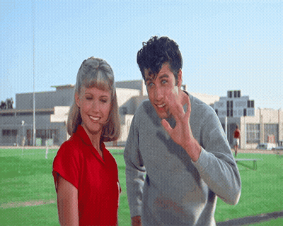 A Man And A Woman Are Standing On A Field And The Man Is Waving GIF