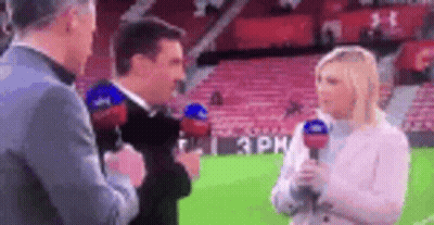 A Man And A Woman Are Standing On A Soccer Field Talking Into Microphones . GIF