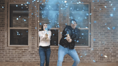 A Man And A Woman Are Throwing Blue Confetti In Front Of A Brick House GIF
