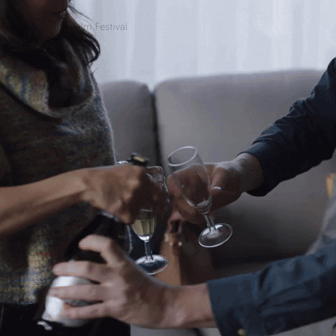 A Man And A Woman Are Toasting With Champagne In Front Of A Film Festival Logo GIF