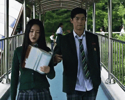 A Man And A Woman Are Walking Across A Bridge And The Woman Is Holding A Book GIF