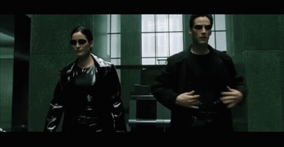 A Man And A Woman Are Walking Down A Hallway With A Sign That Says Exit On It GIF