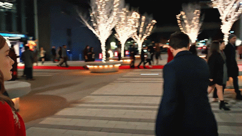 A Man And A Woman Are Walking Down A Sidewalk In Front Of A Sign That Says ' Abercrombie & Fitch ' GIF