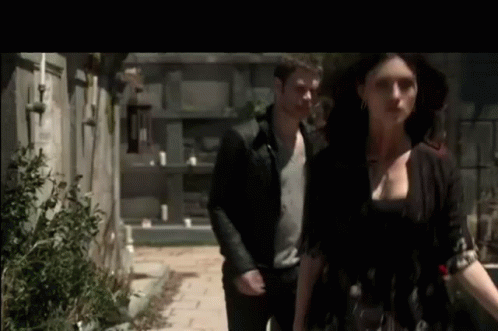 A Man And A Woman Are Walking Down A Sidewalk Next To Each Other . GIF