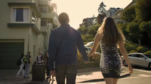 A Man And A Woman Are Walking Down A Street With A Sign That Says No Parking GIF