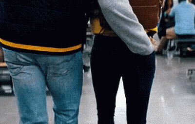A Man And A Woman Are Walking In A Hallway Holding Hands GIF