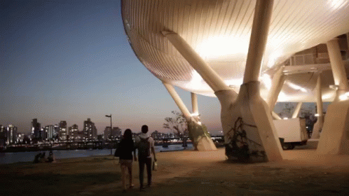 A Man And A Woman Are Walking In Front Of A Building GIF
