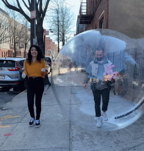 A Man And A Woman Are Walking Through A Clear Bubble On A Sidewalk With A No Parking Sign In The Background GIF