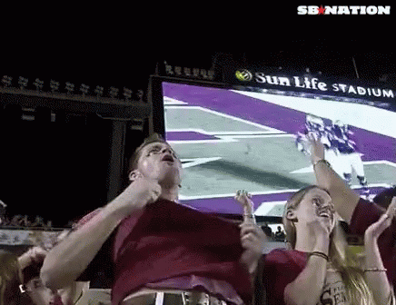 A Man And A Woman Are Watching A Football Game At Sun Life Stadium GIF