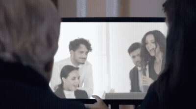 A Man And A Woman Are Watching A Group Of People On A Television Screen . GIF