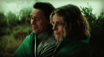 A Man And A Woman Are Wrapped In A Green Blanket And Looking At Each Other . GIF