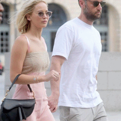 A Man And A Woman Holding Hands While Walking Down A Street GIF