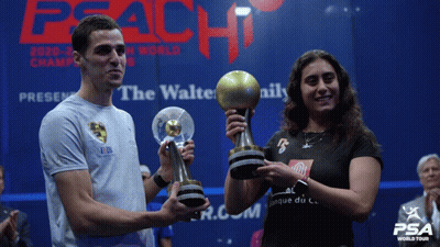 A Man And A Woman Holding Trophies In Front Of A Peach World Tour Sign GIF