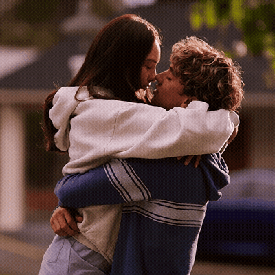 A Man And A Woman Hugging And Kissing In Front Of A Building GIF