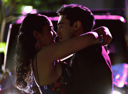 A Man And A Woman Hugging And Kissing In Front Of A Car GIF