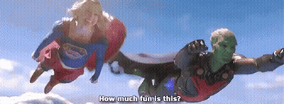 A Man And A Woman In Superhero Costumes Are Flying In The Air . GIF