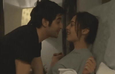 A Man And A Woman Kissing In Bed With A Lamp In The Background GIF