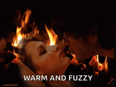 A Man And A Woman Kissing In Front Of A Fire With The Words Warm And Fuzzy Below Them GIF