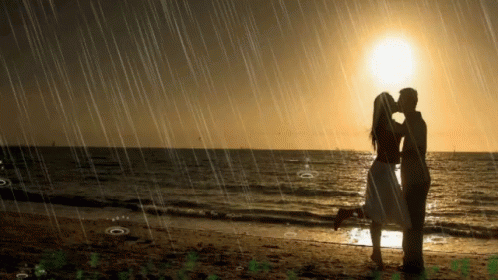 A Man And A Woman Kissing On A Beach In The Rain GIF