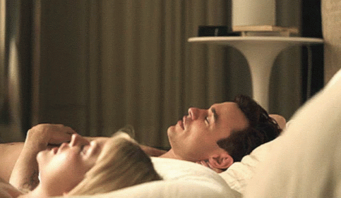 A Man And A Woman Laying On A Bed With Their Eyes Closed GIF