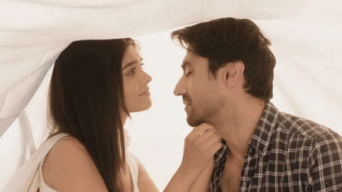 A Man And A Woman Looking At Each Other Under A White Curtain GIF