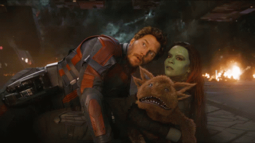A Man And A Woman Looking At Each Other With A Stuffed Animal Between Them GIF