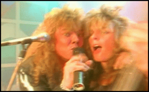 A Man And A Woman Singing Into Microphones In A Blurry Photo GIF