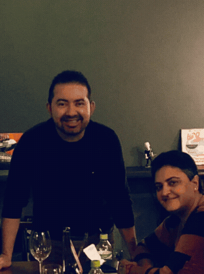 A Man And A Woman Sit At A Table In Front Of A Sign That Says B20 On It GIF